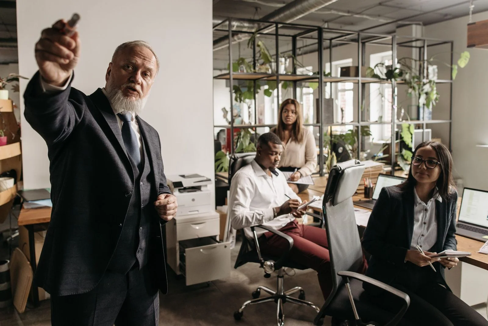 Un equipo diverso reunido alrededor de una mesa en una oficina moderna y luminosa mientras un líder senior presenta.