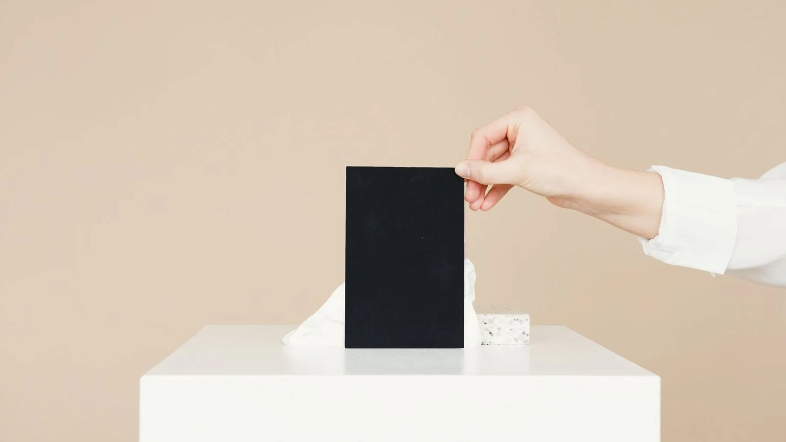 A hand holds a black card against a plain beige background with open space.