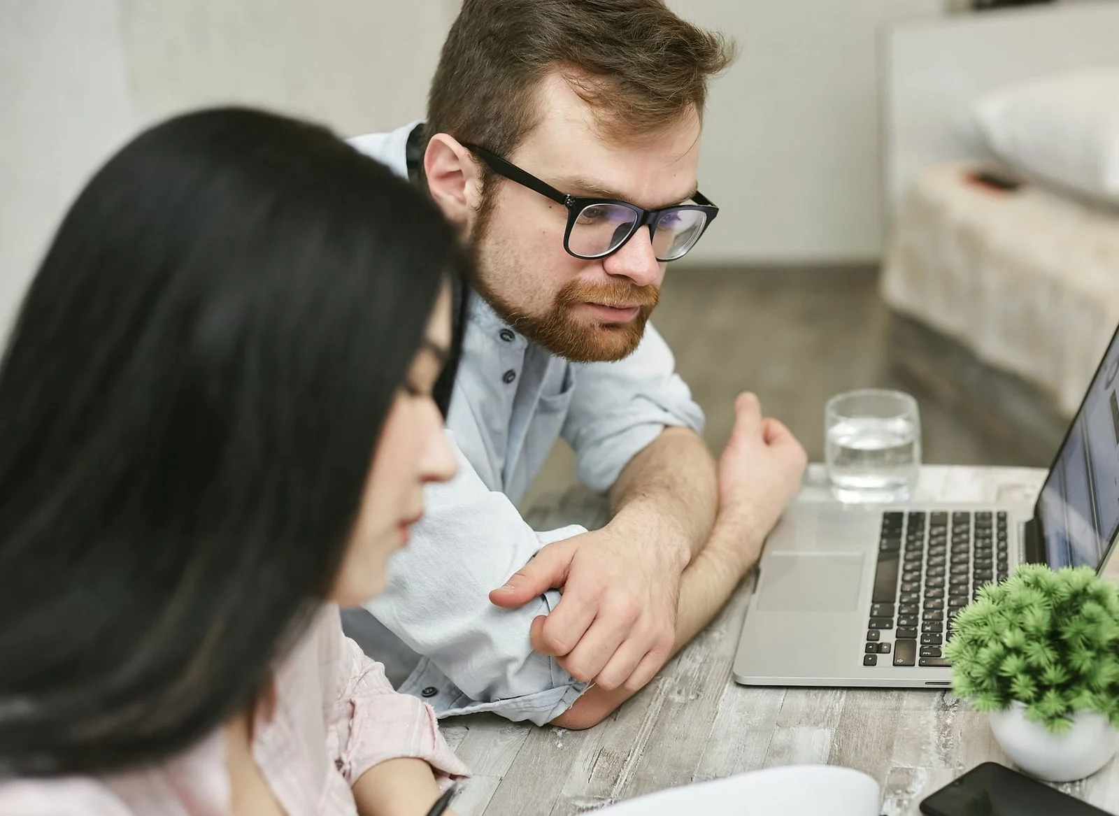 A man and a woman review documents together on a laptop at an indoor table.