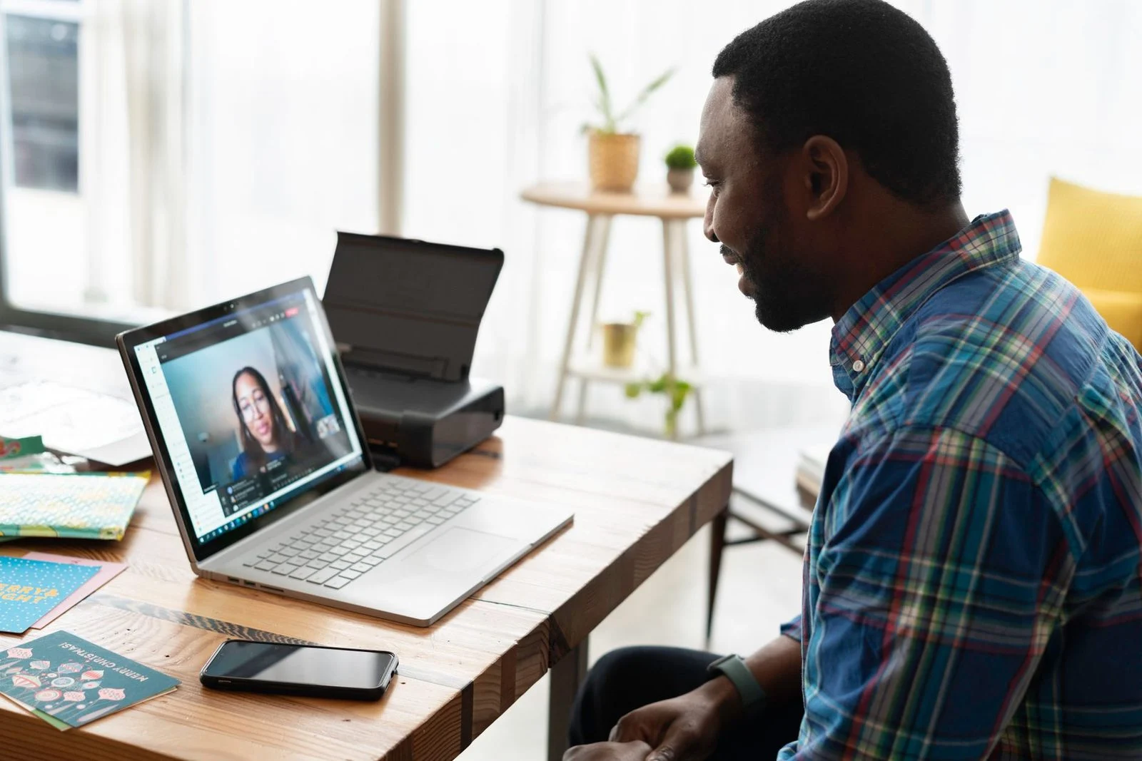 A man on a video call with a colleague at a wooden desk in a modern office.