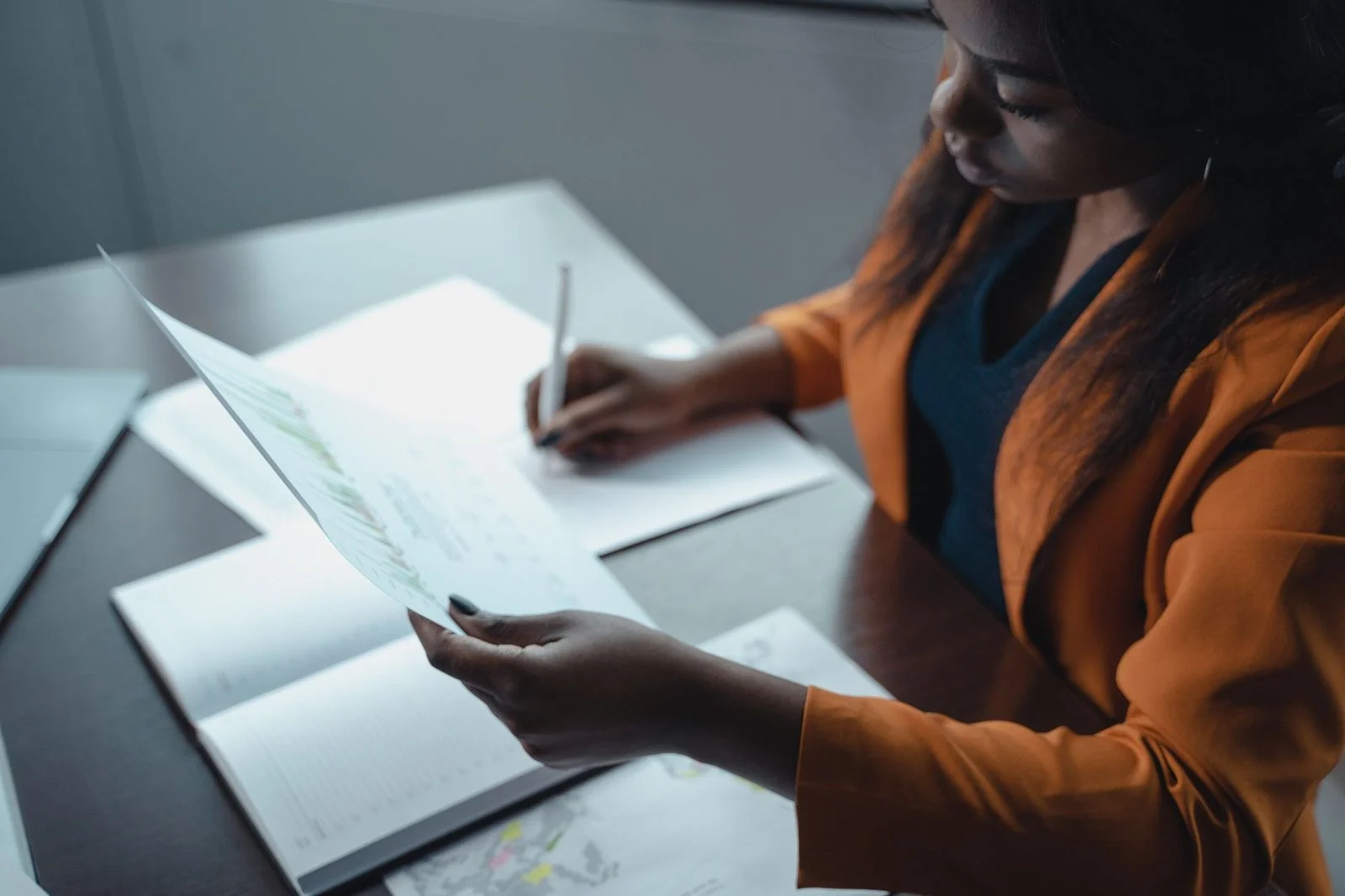 A professional woman in office attire reviews documents at her desk.