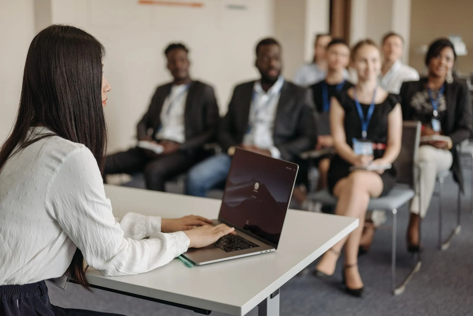 A professional woman presents to a diverse group of colleagues in a bright office meeting room.