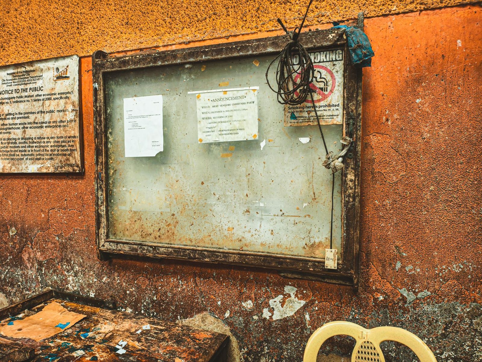 A rustic notice board with pinned announcements against a textured orange wall.