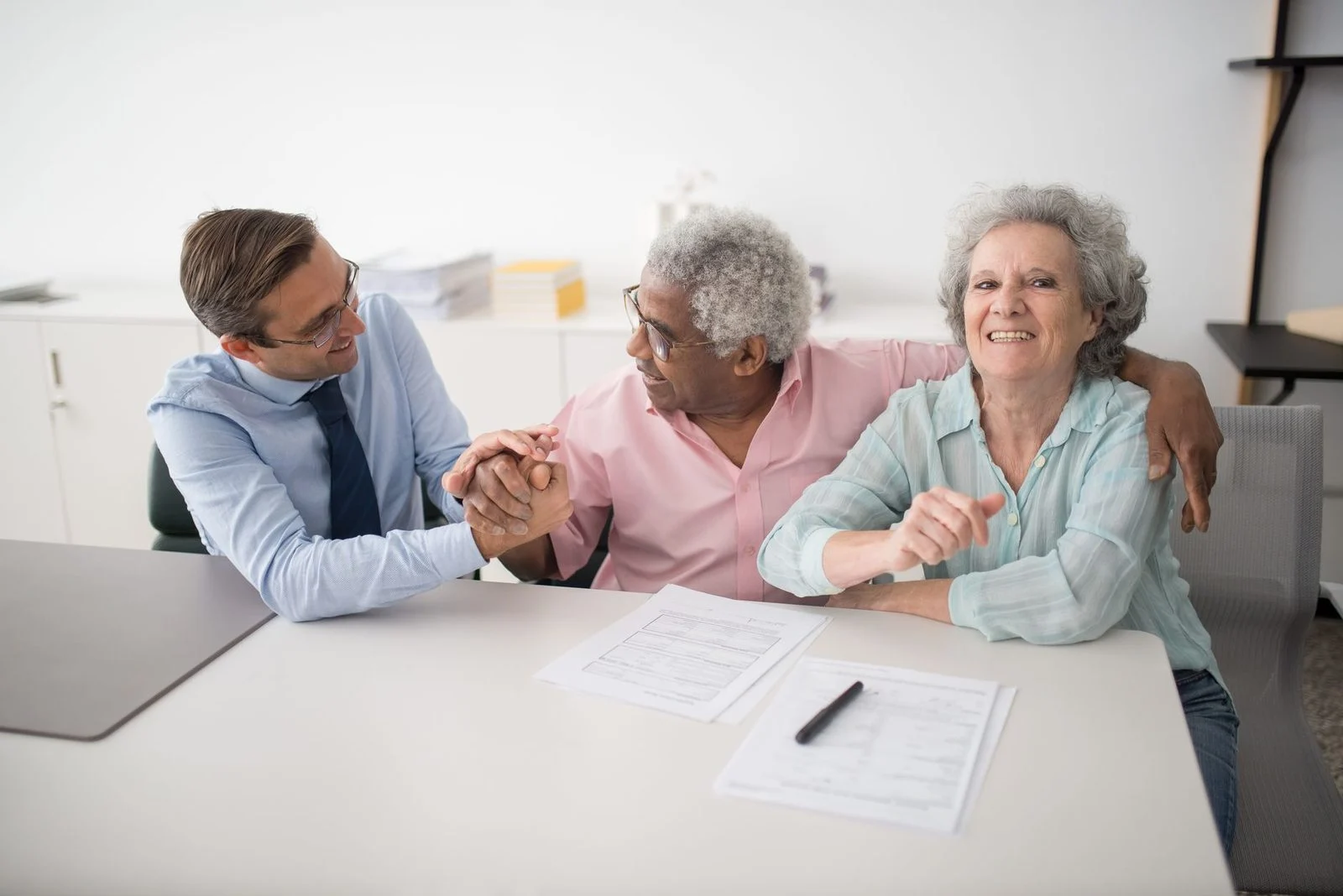 A senior couple smiles as they review financial documents with a consultant in an office.