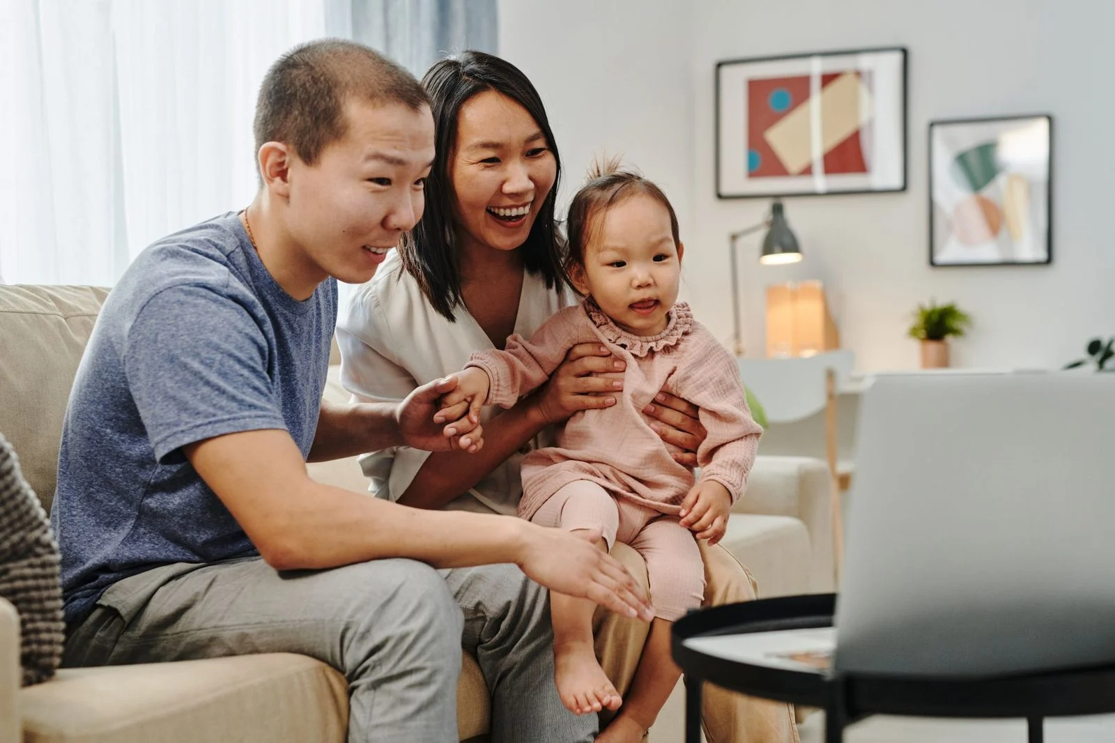 A smiling Asian family sits together on a couch during a video call.