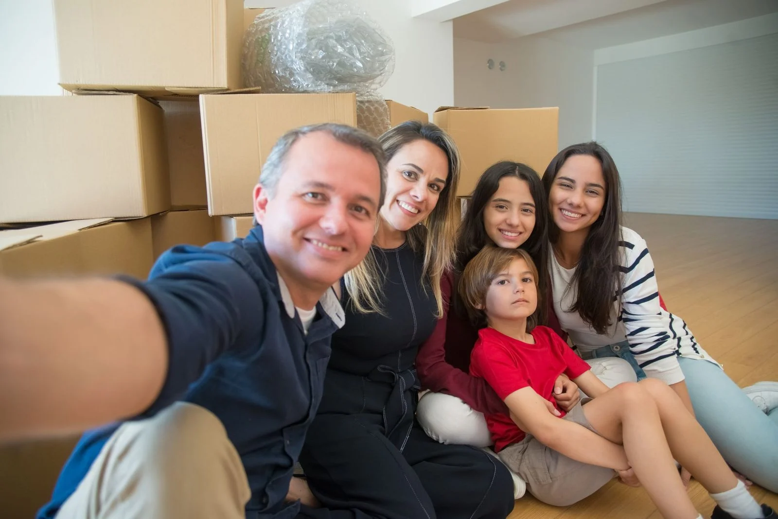 A smiling family takes a selfie together among moving boxes in their new home.