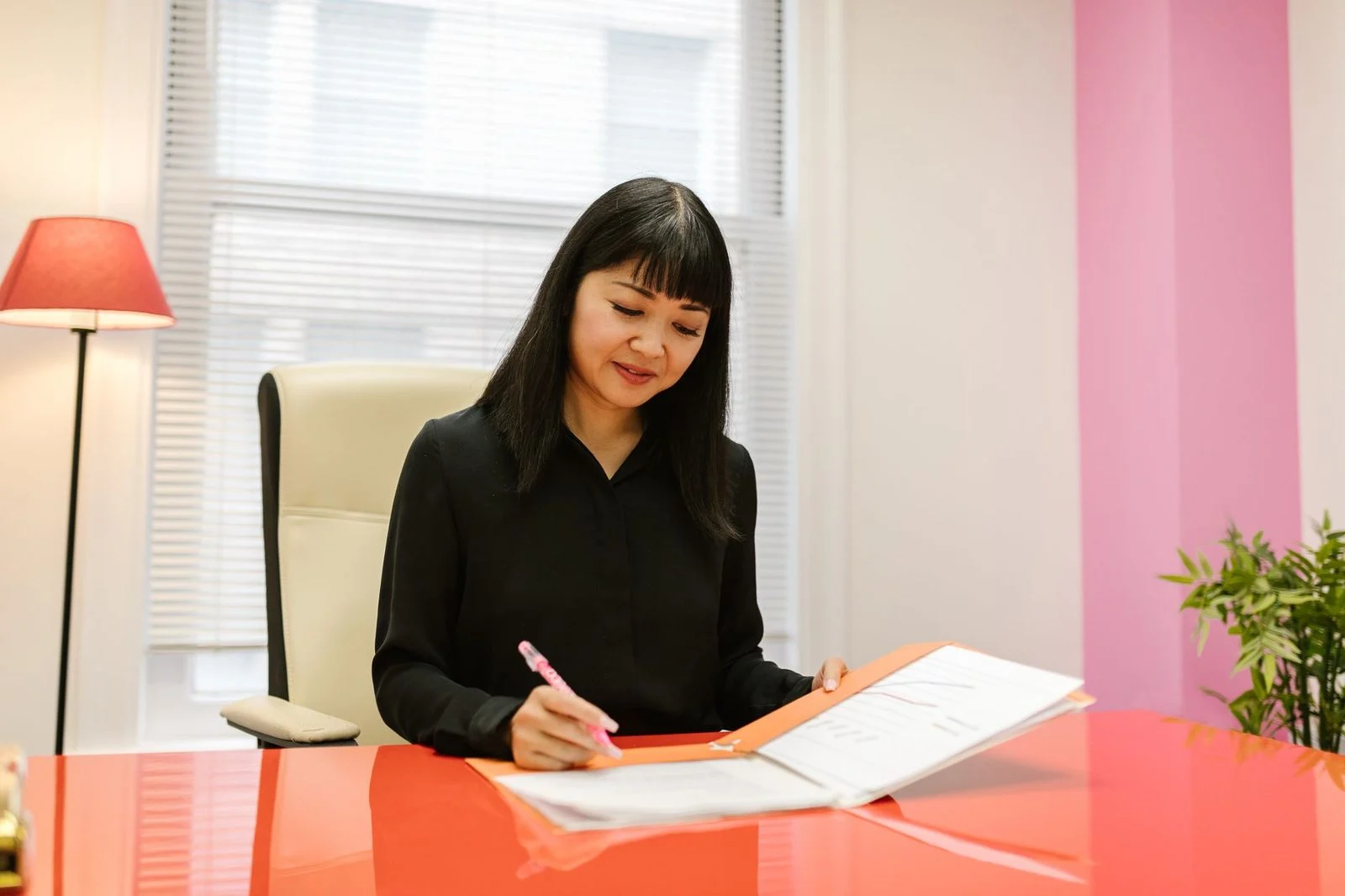 A woman in a bright, modern office reviews paperwork at her desk.