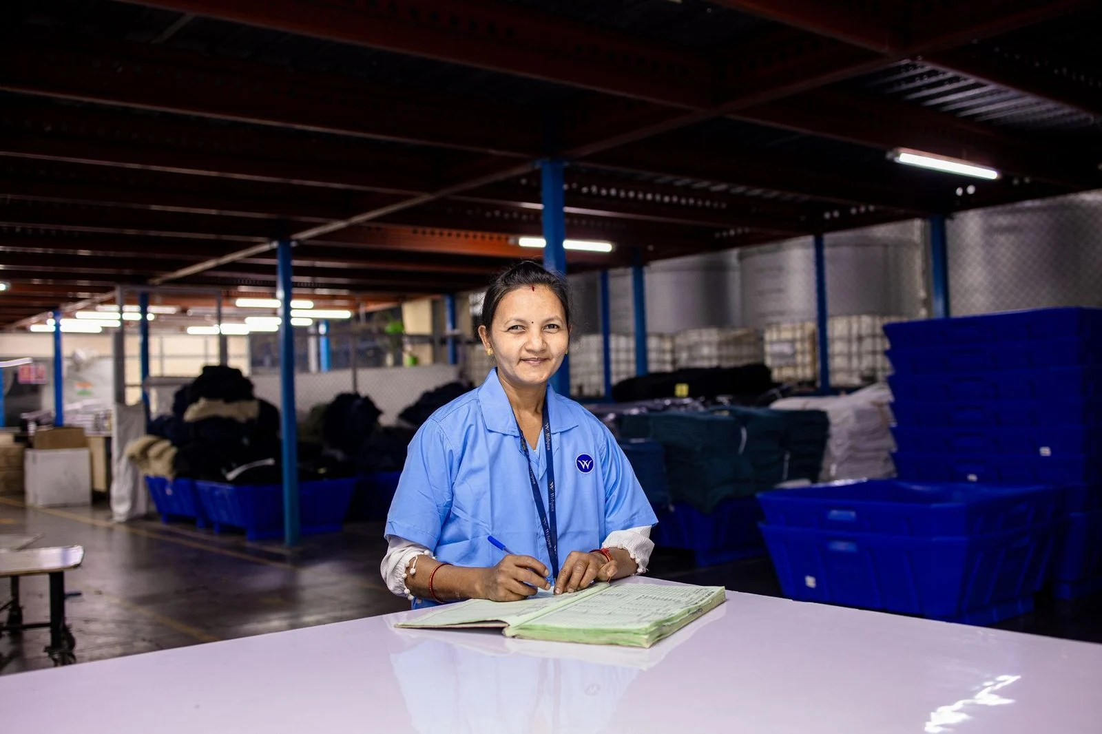 A woman in a uniform writes in a notebook inside a textile warehouse.