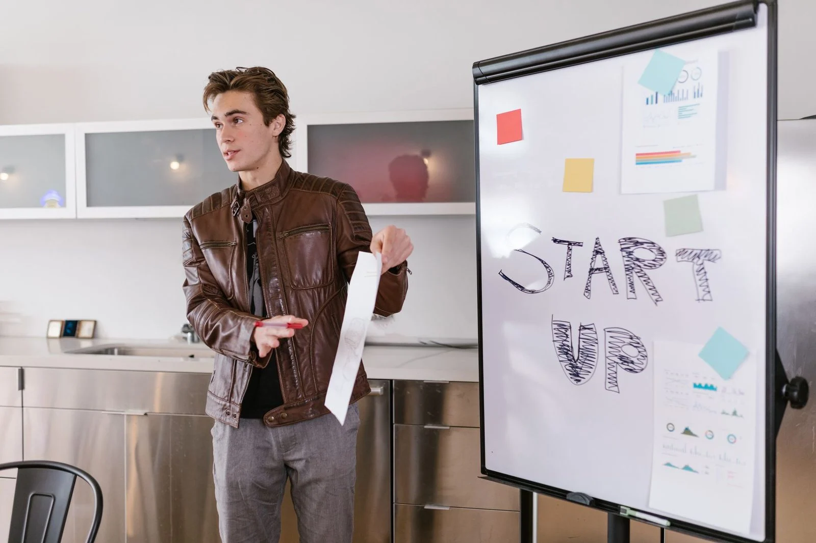 Joven emprendedor presenta estrategias de startup junto a un rotafolio en una sala de reuniones.
