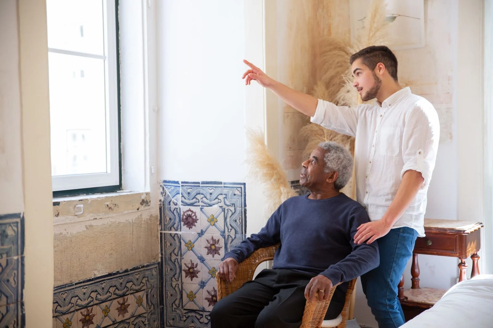 A young man points out a view to an elderly man in a living room decorated in Portuguese style.