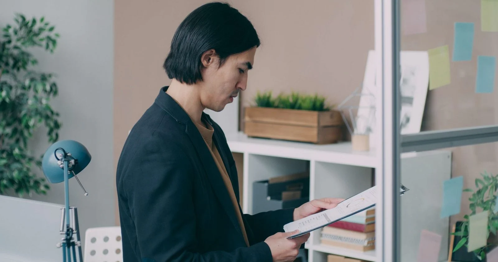 A young man reviews paperwork at a desk in a modern office.