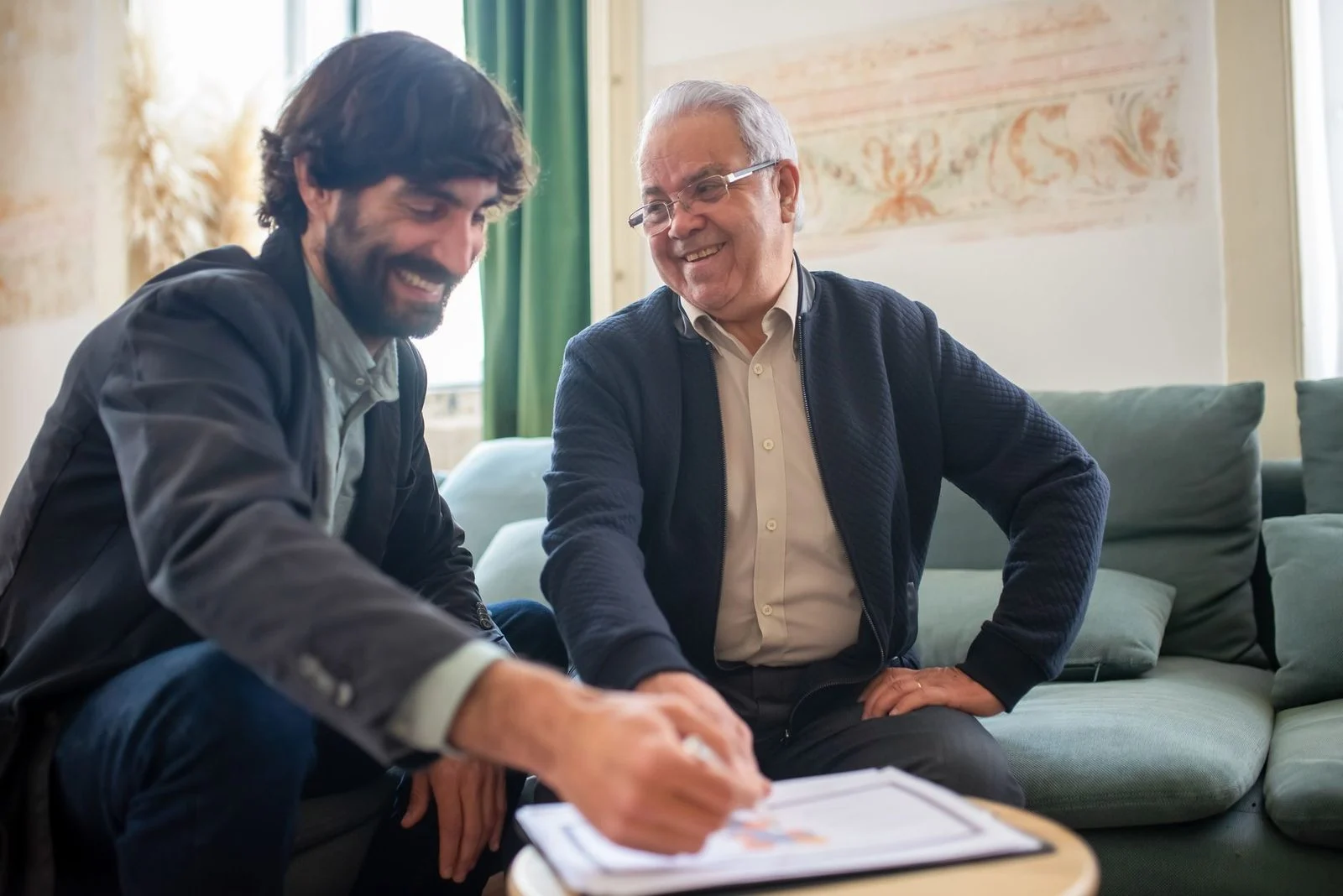 An advisor reviews documents with an elderly client during an indoor consultation.