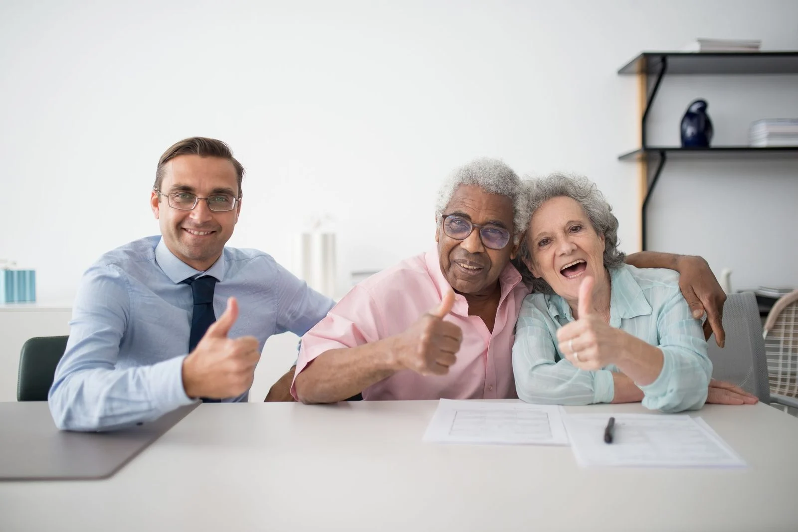 Una pareja de adultos mayores sonriente levanta el pulgar mientras se reúne con un asesor en una oficina.