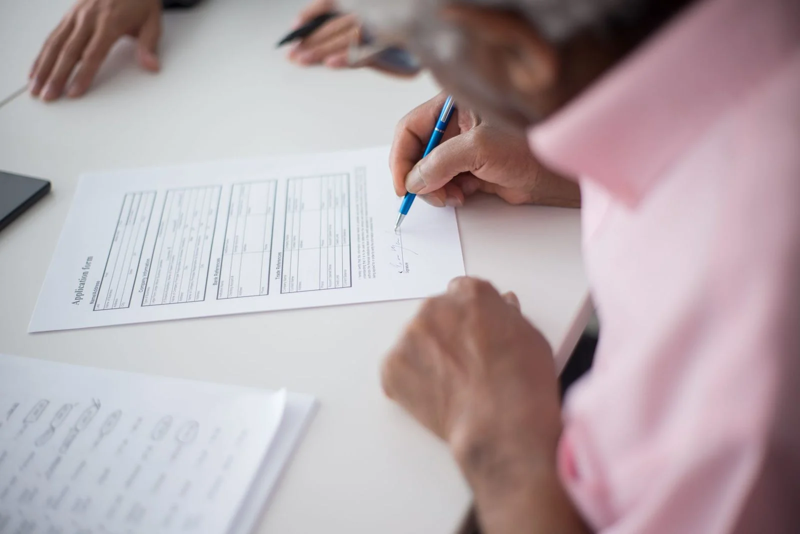 Elderly man signs a business document at an office desk.