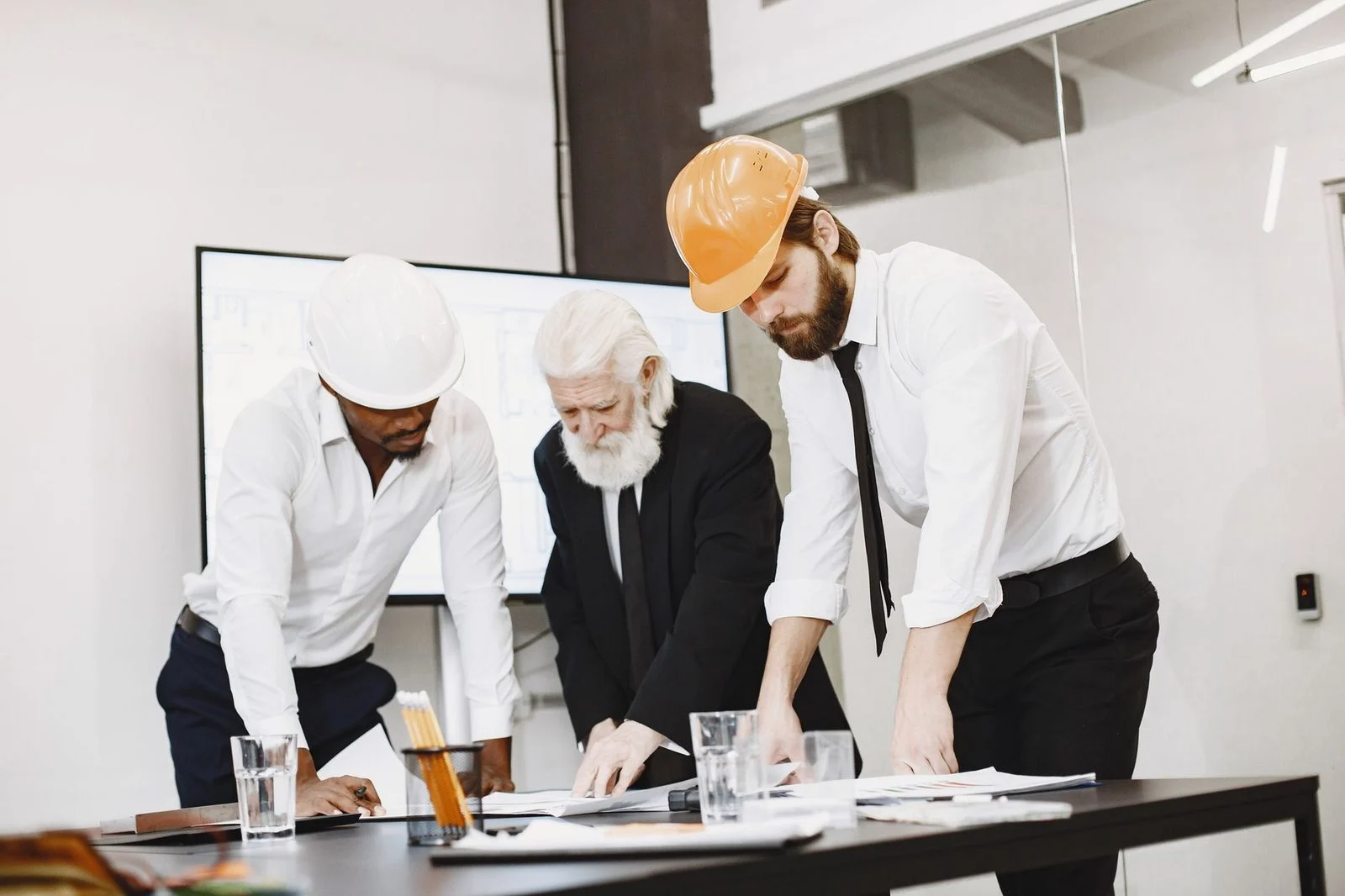 Arquitectos con cascos revisan juntos planos de construcción en una oficina moderna.