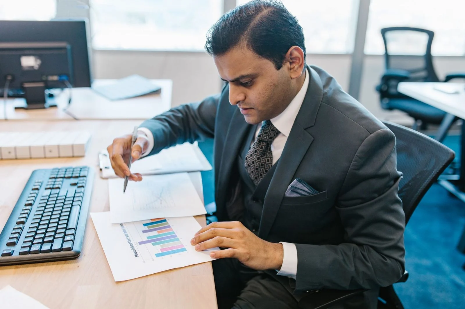 Business professional reviewing graphs and charts at a desk in a modern office.
