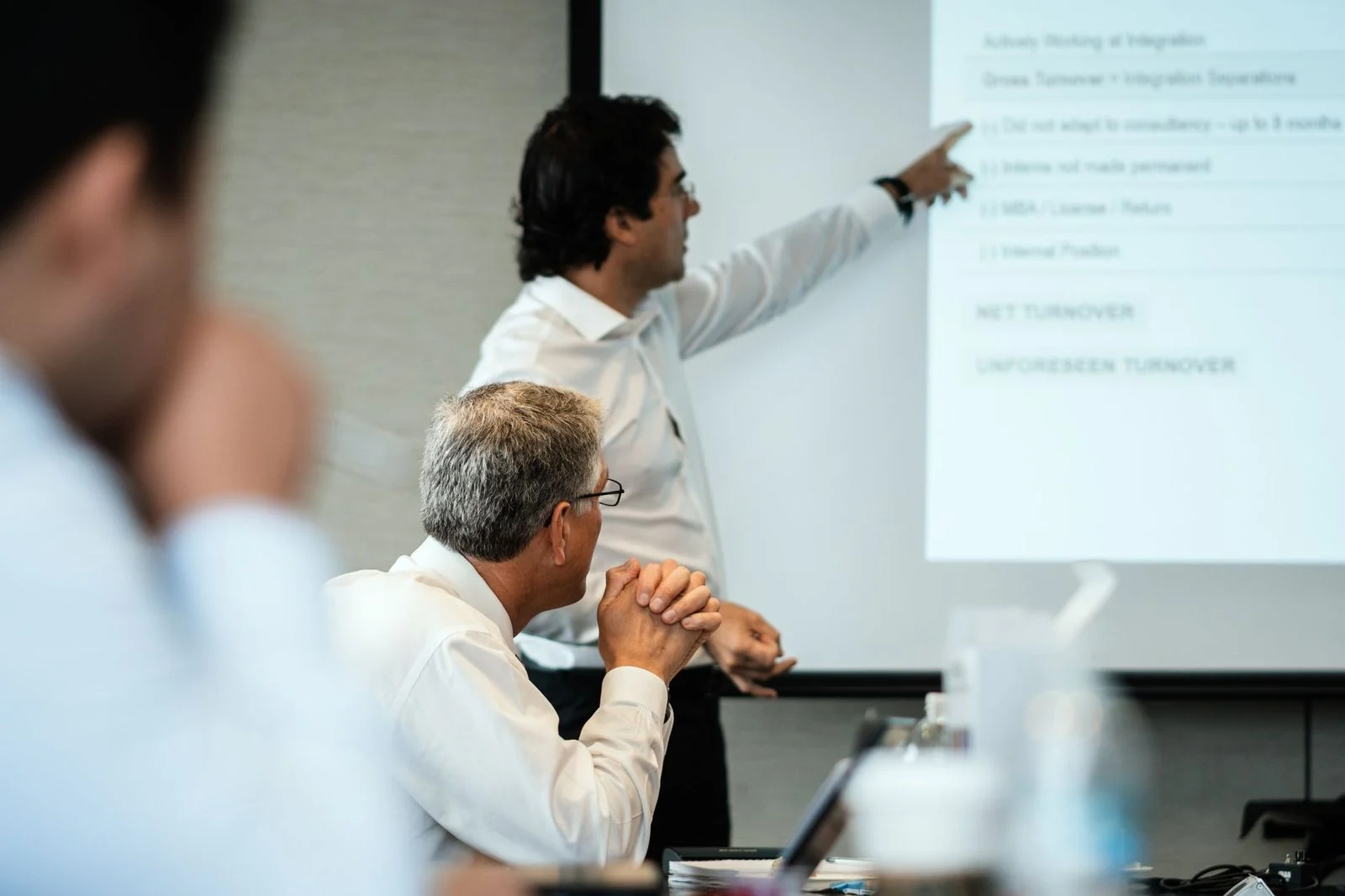 Business team members gather attentively around a presentation during a meeting in a professional office.