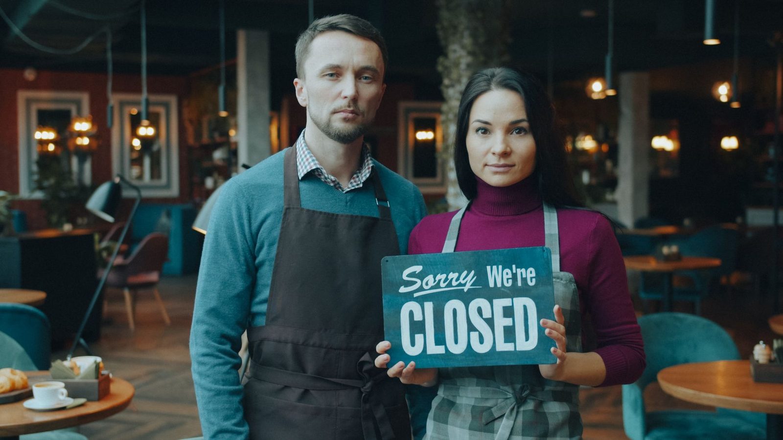 Café owners holding a closed sign in their restaurant.