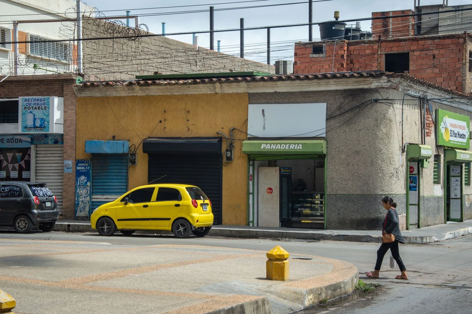 Calle urbana con un auto amarillo estacionado frente a una panadería y edificios de arquitectura típica de la ciudad.