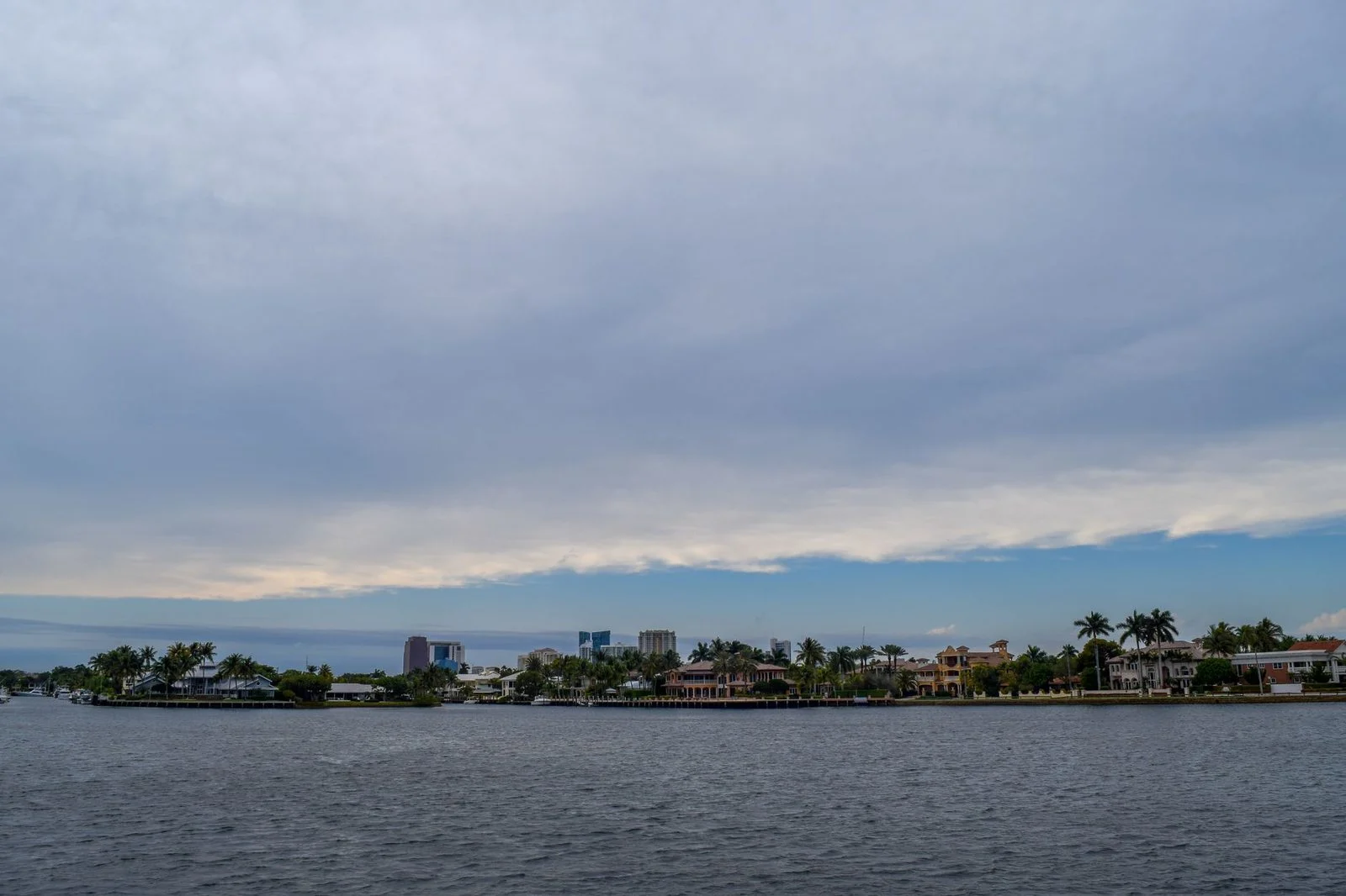 Casas de lujo frente al mar con palmeras en Fort Lauderdale bajo cielo nublado.