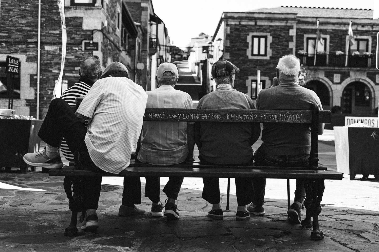 Cinco hombres mayores sentados en un banco en el centro histórico de Santiago.