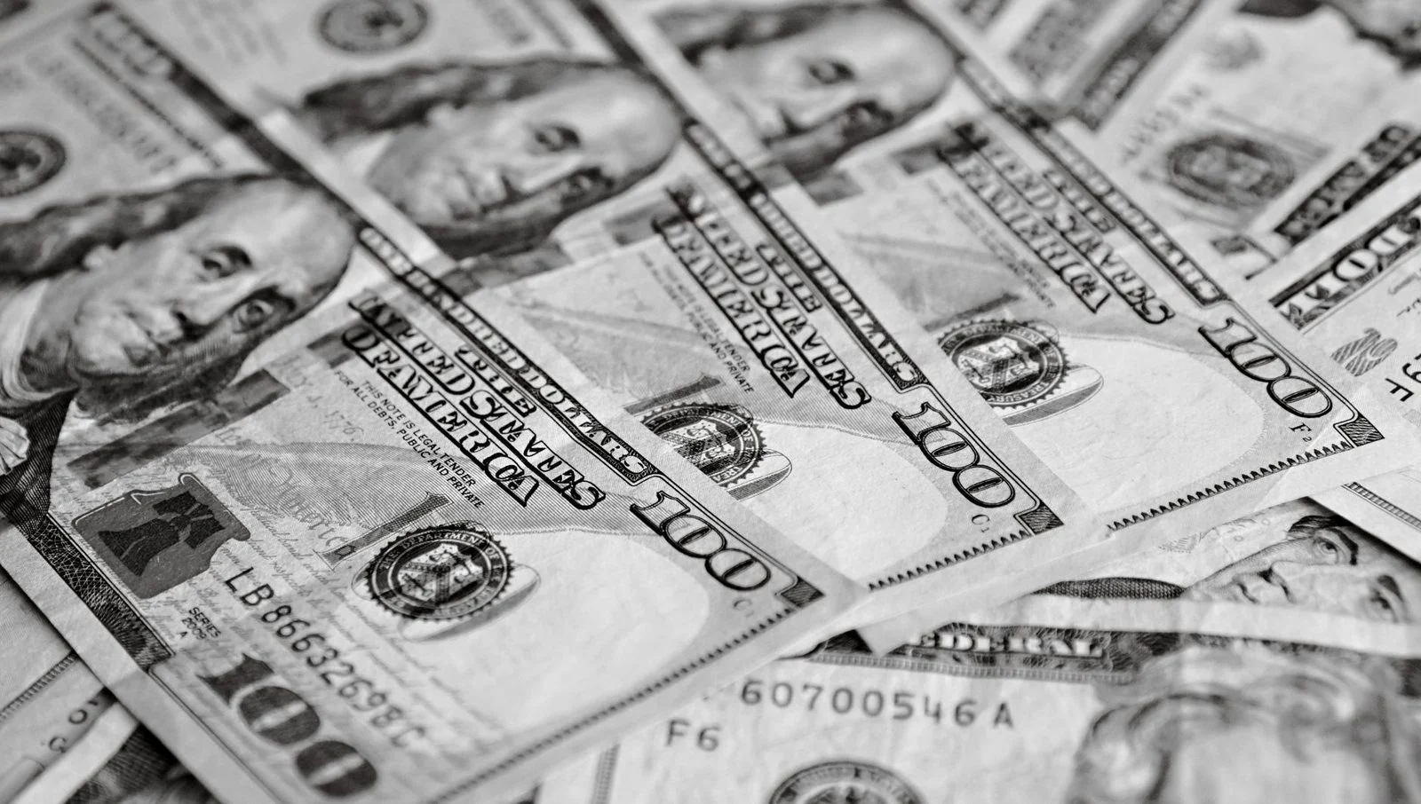 Primer plano en blanco y negro de billetes de cien dólares estadounidenses esparcidos.