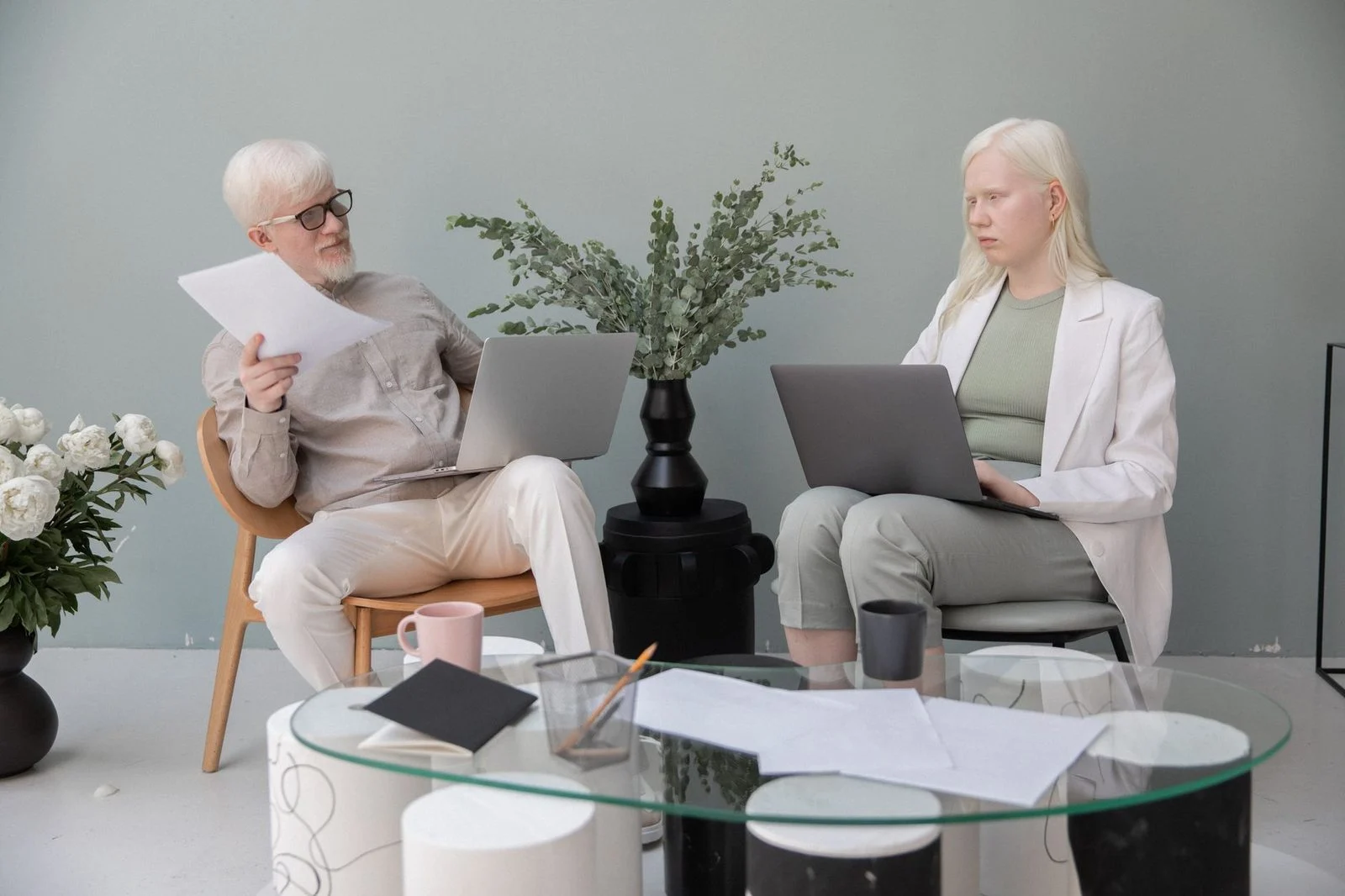 Colegas concentrados en sus computadoras en una mesa de cristal junto a una planta en una oficina luminosa.