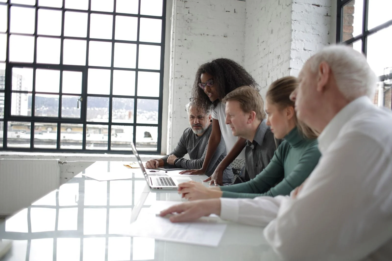 Colleagues gather around a laptop at a table in a modern office, focused on a project together.