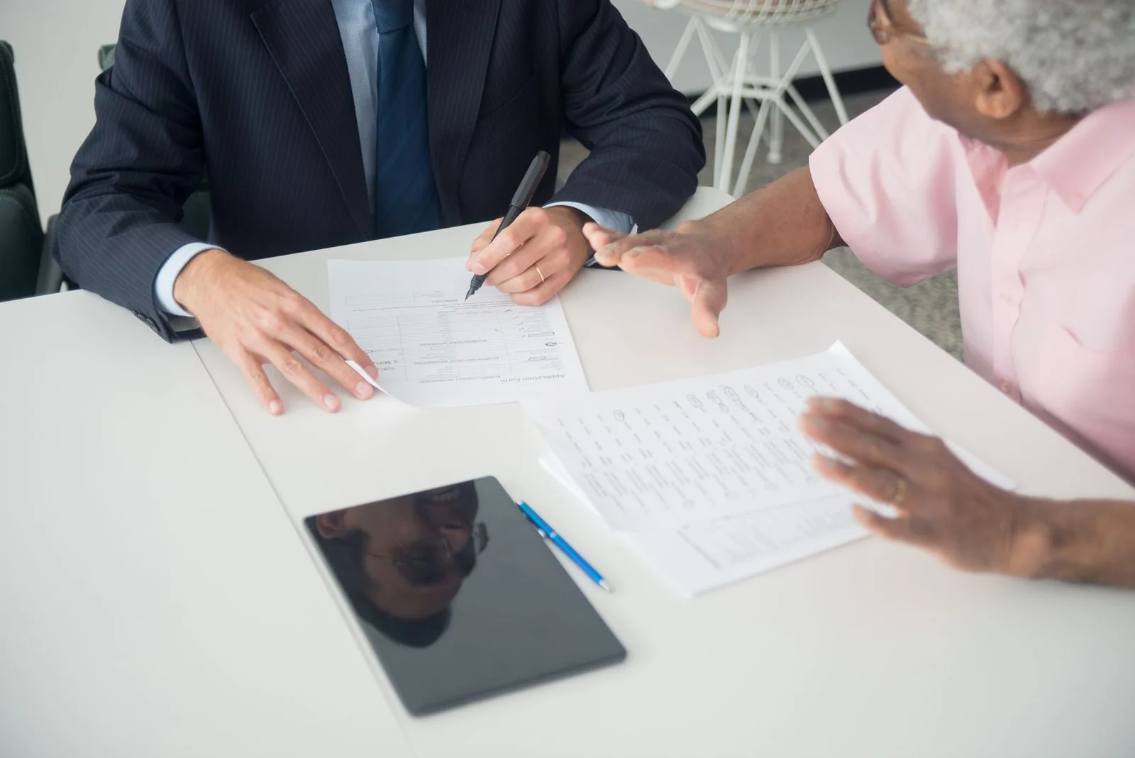 A consultant and an elderly client review documents together across an office table.