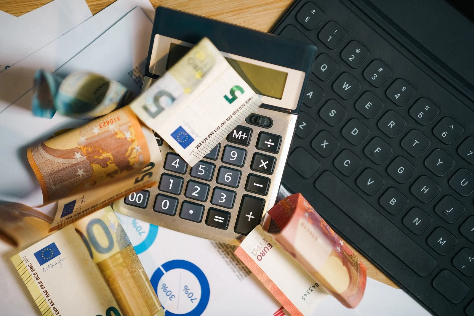 Billetes de euro, una calculadora y un teclado de portátil dispuestos sobre un escritorio para contabilidad empresarial.