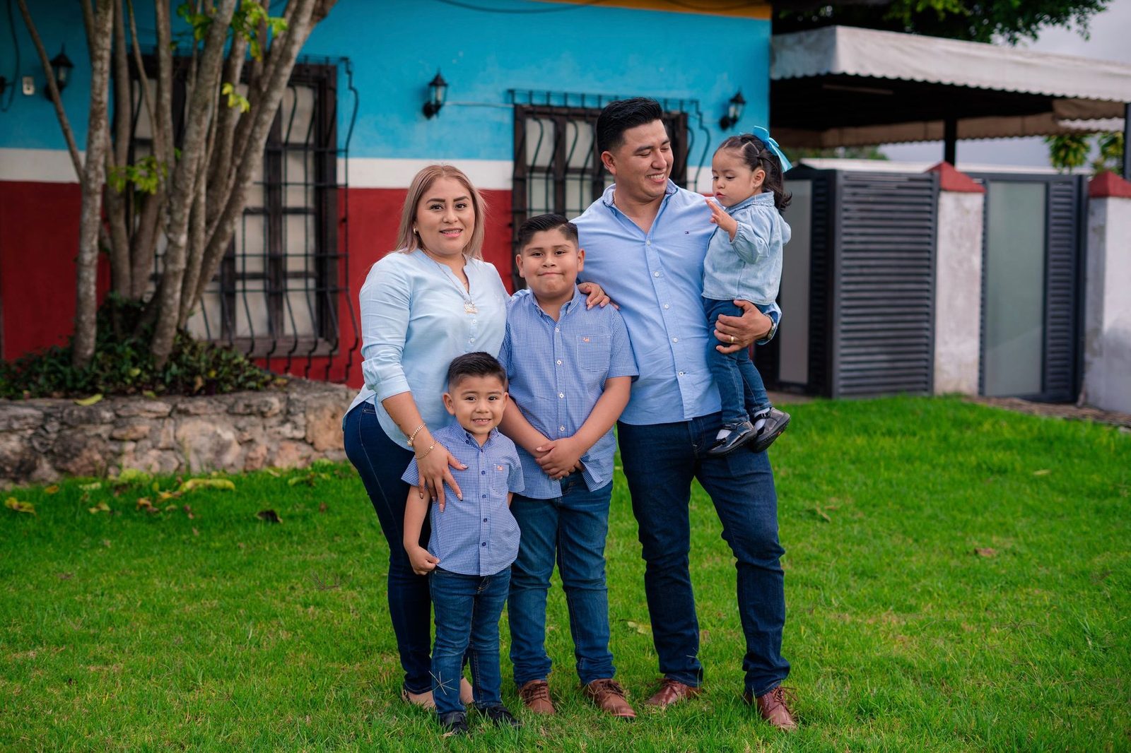 Familia sonriendo juntos en el jardín frente a casa moderna.