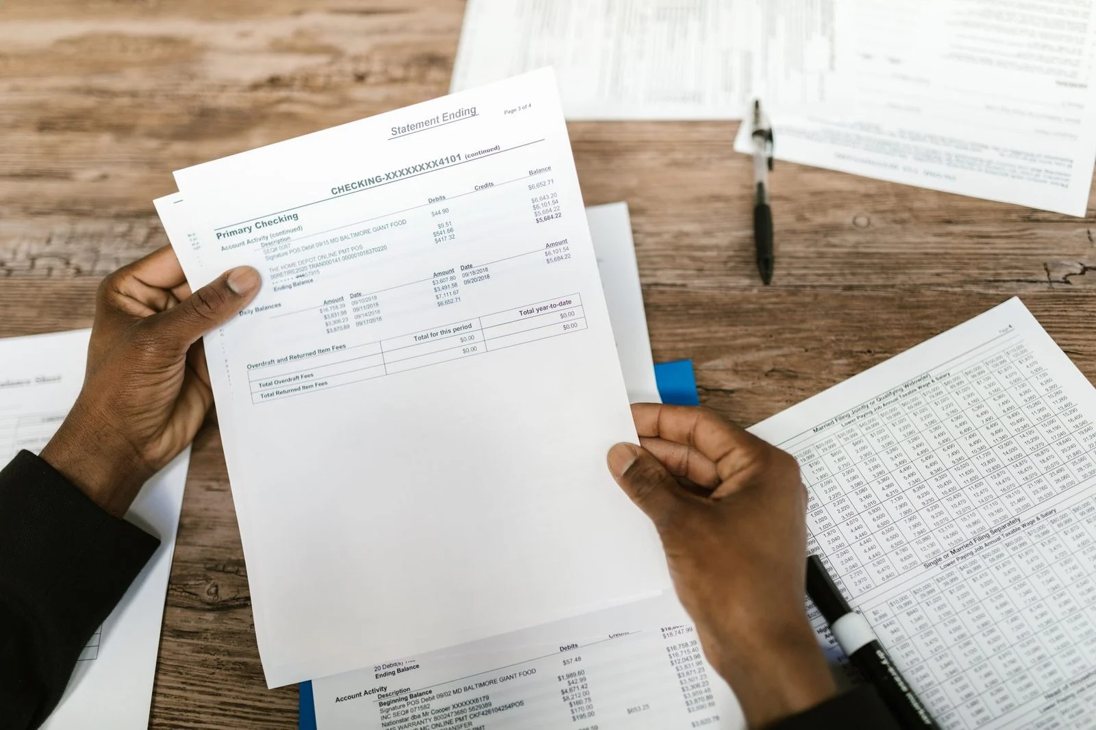 Hands holding financial papers and tax forms spread across a desk for review.