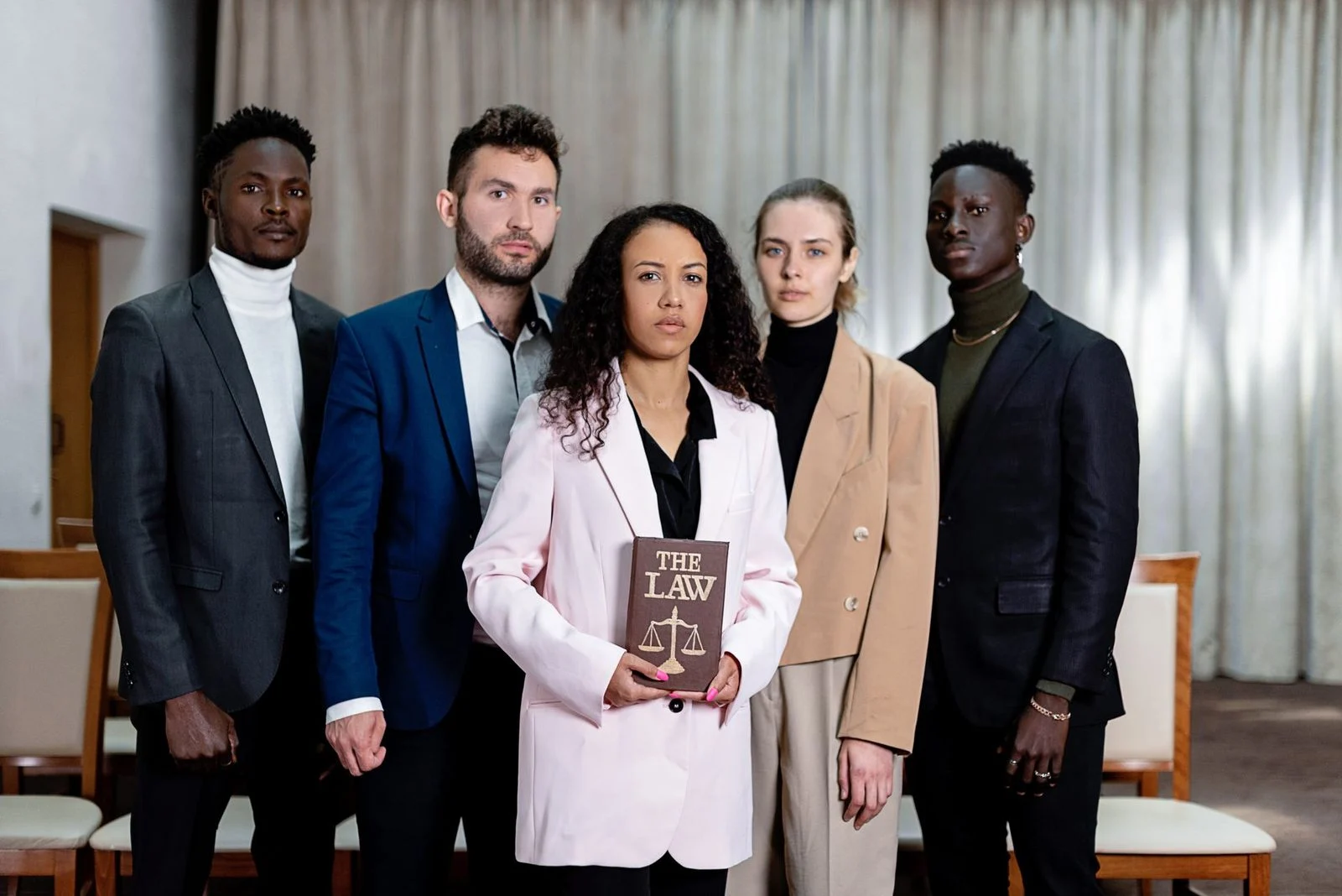 Five diverse lawyers stand confidently in an office, one holding a law book.