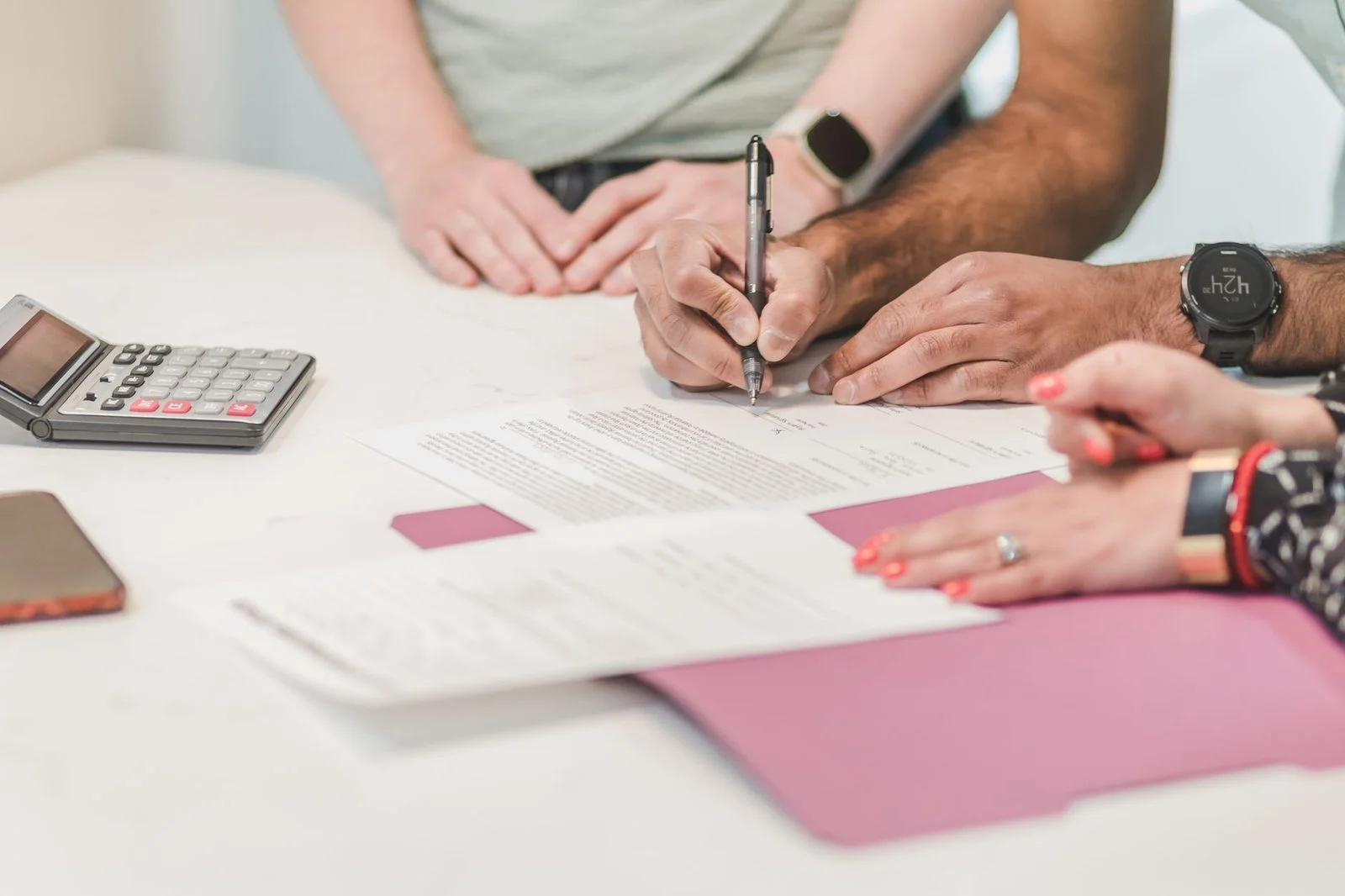 Four colleagues review paperwork and use a calculator at a white table.