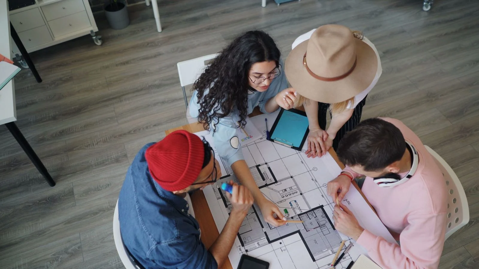 Four people gather around architectural blueprints on a table in a modern office.