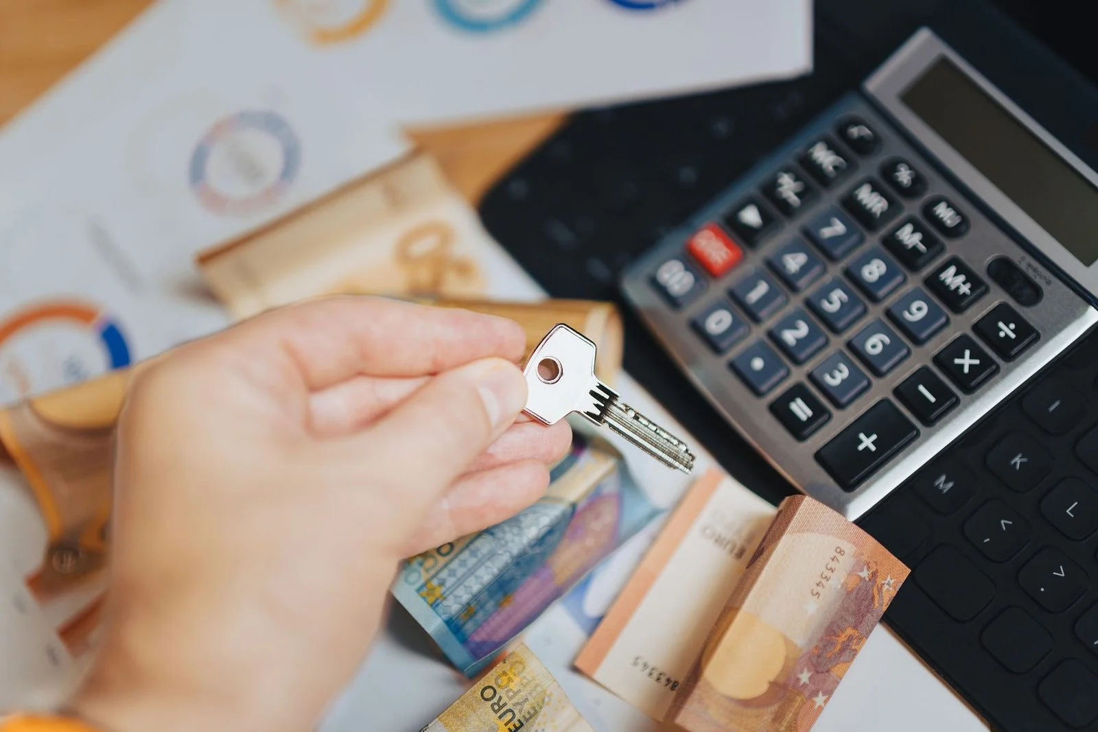 Mano sosteniendo una llave sobre billetes de euro y una calculadora.