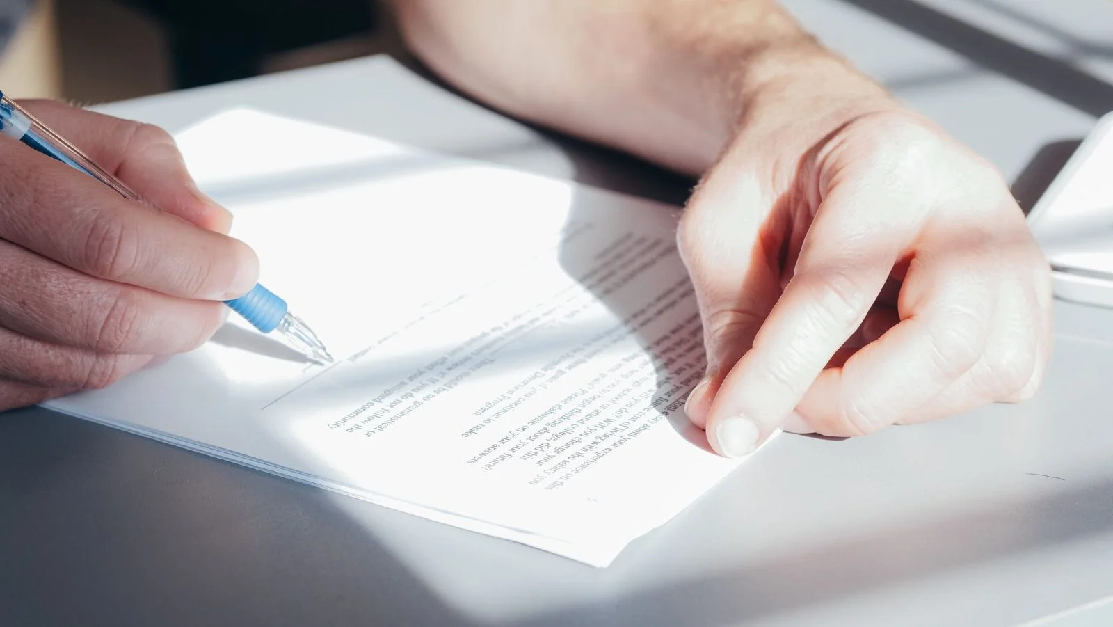 Manos firmando un documento con un bolígrafo azul en primer plano.