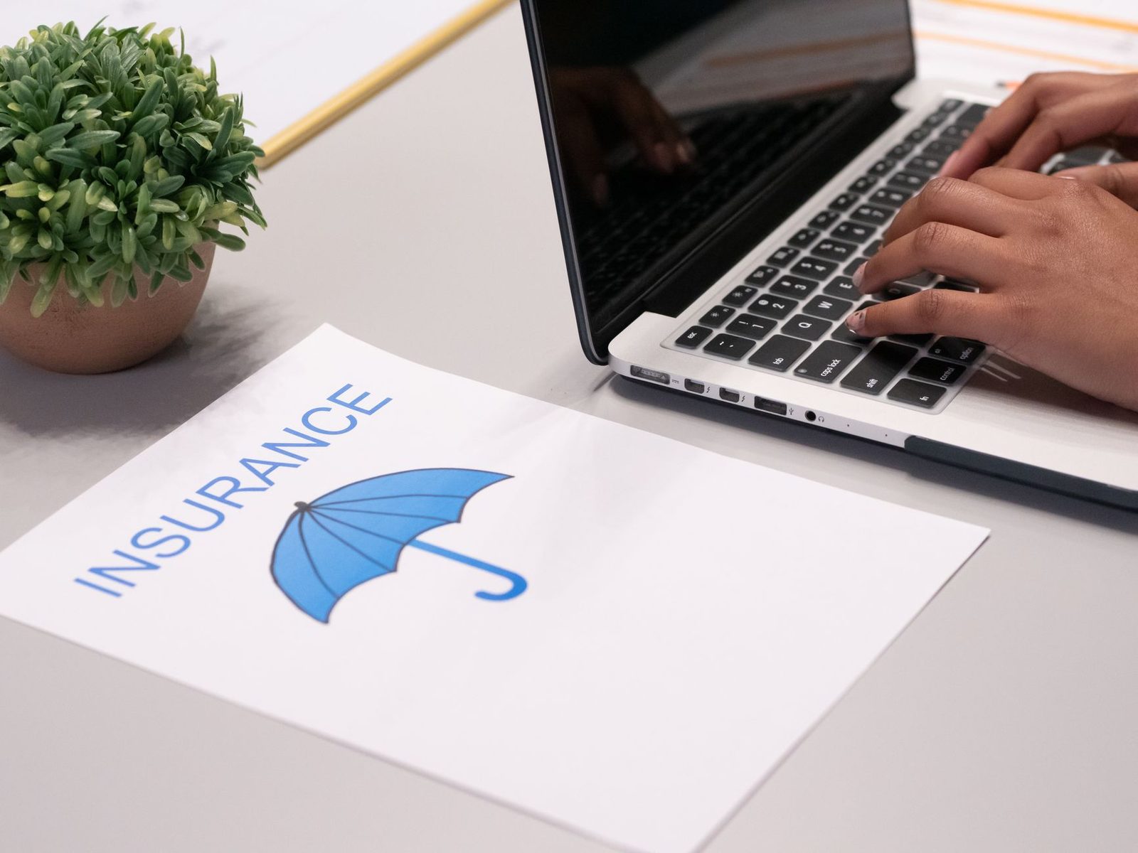 Hands typing on laptop with insurance document on desk.