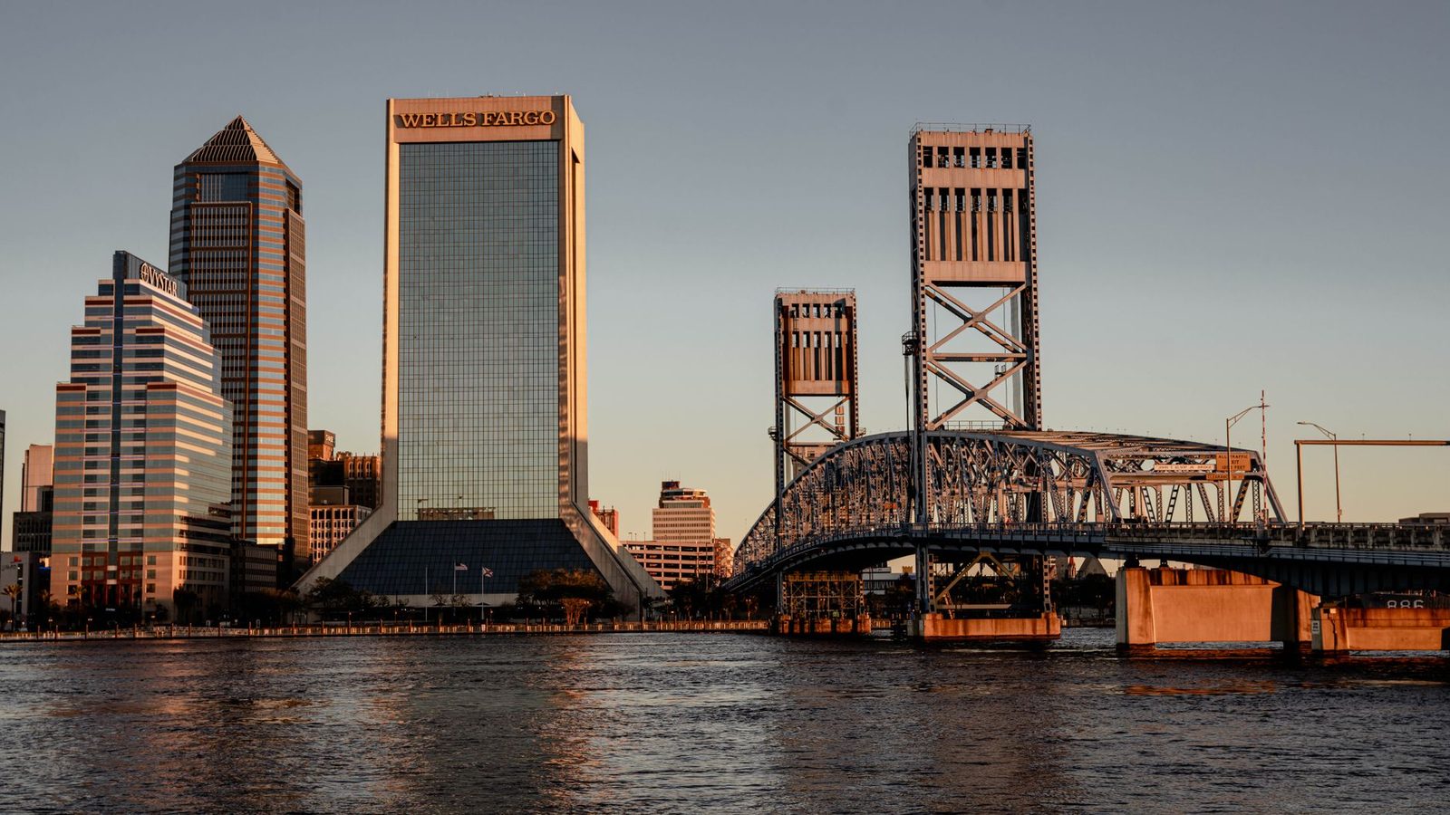 Horizonte de Jacksonville al atardecer con puentes icónicos y rascacielos reflejados en el agua.
