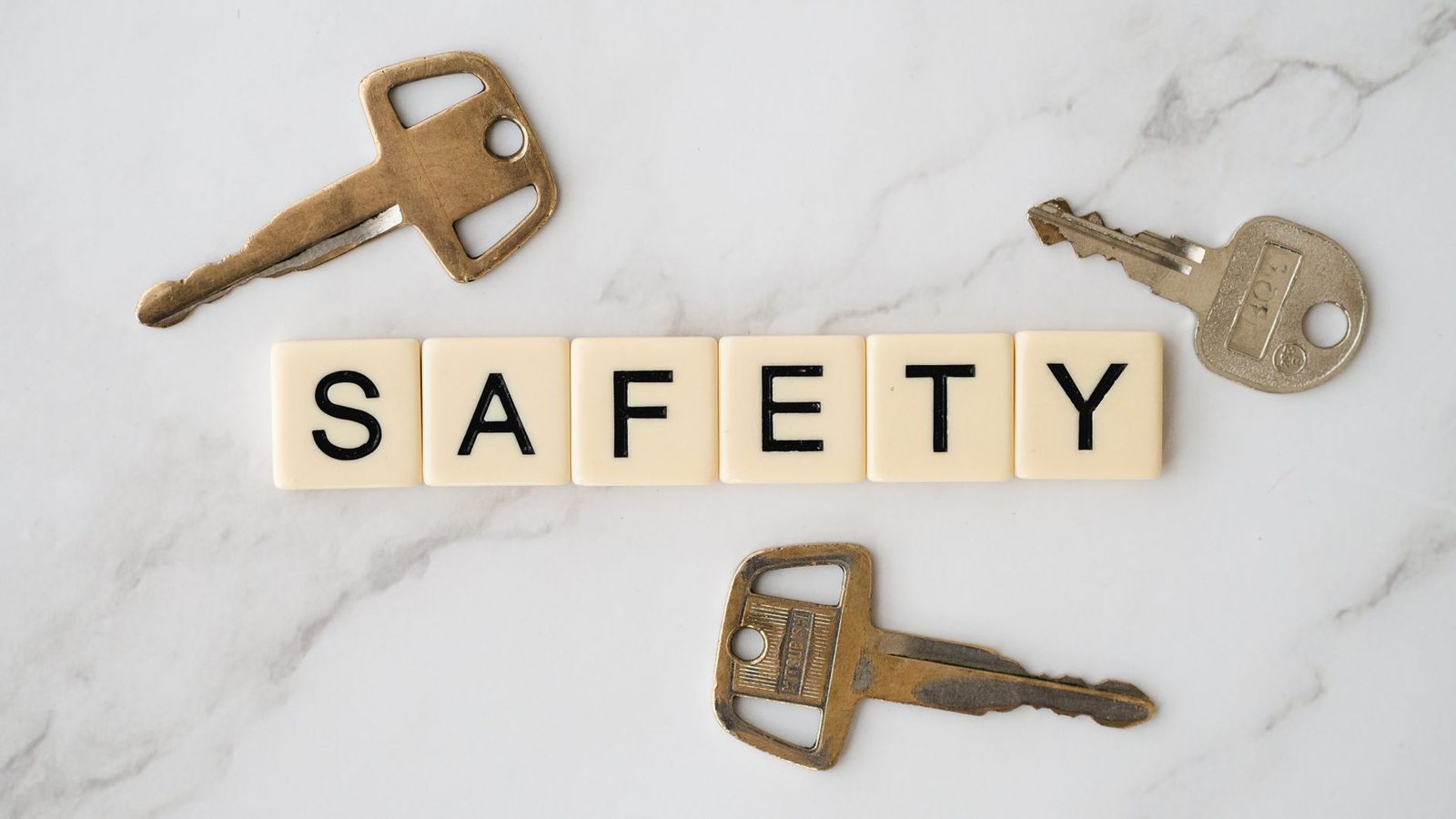 Keys and scrabble tiles spelling "safety" on marble surface.