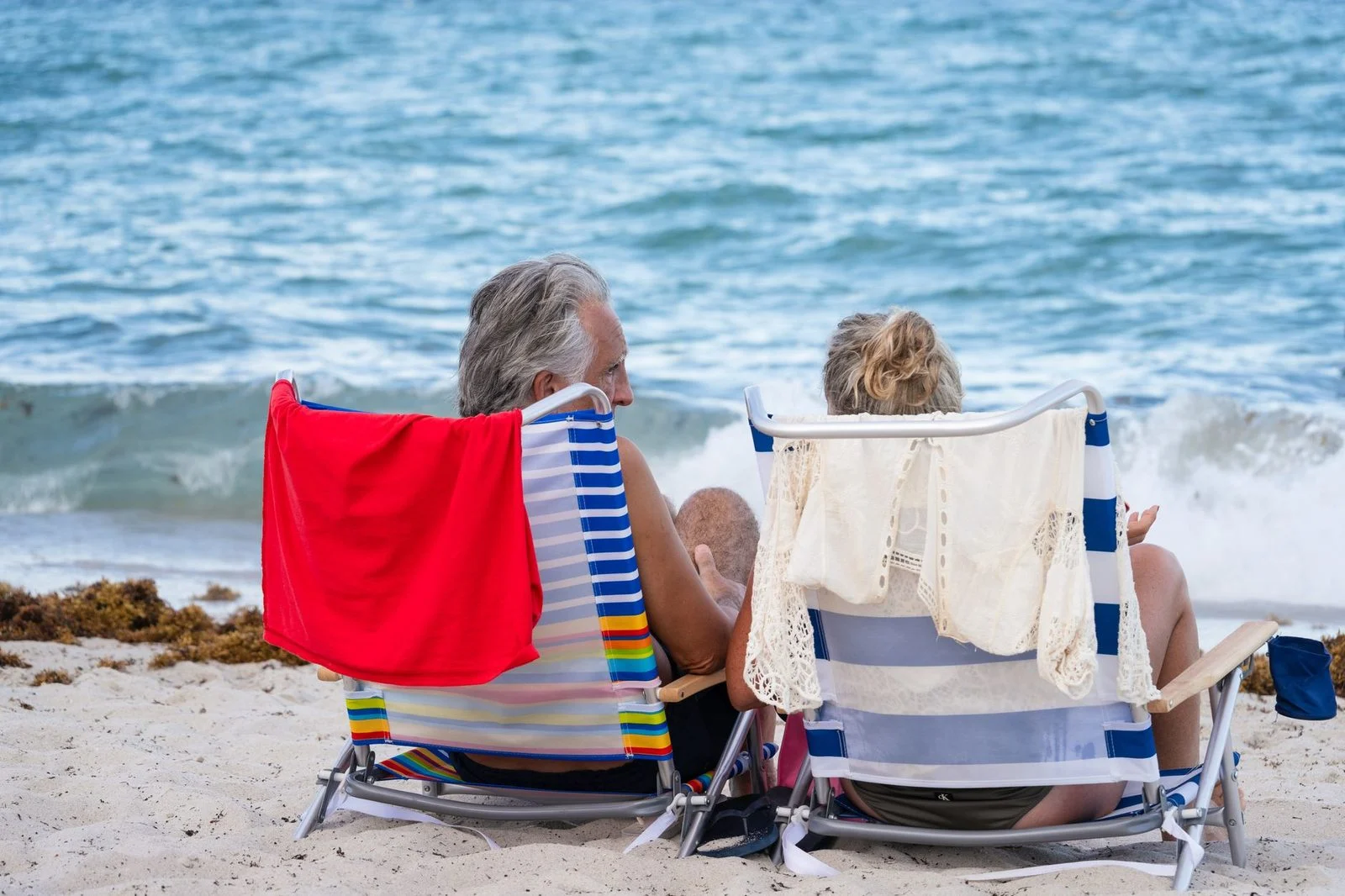 Pareja de adultos mayores latinos sentados en una playa de Miami, disfrutando de la vista al océano bajo el sol de verano.