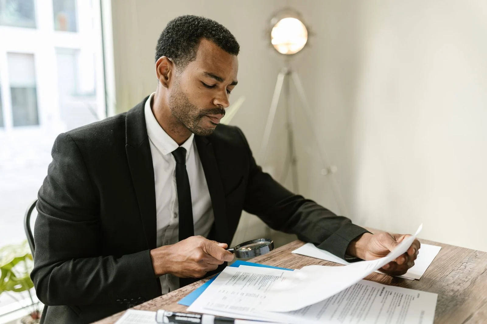 Professional man examines paperwork with a magnifying glass at an office desk.