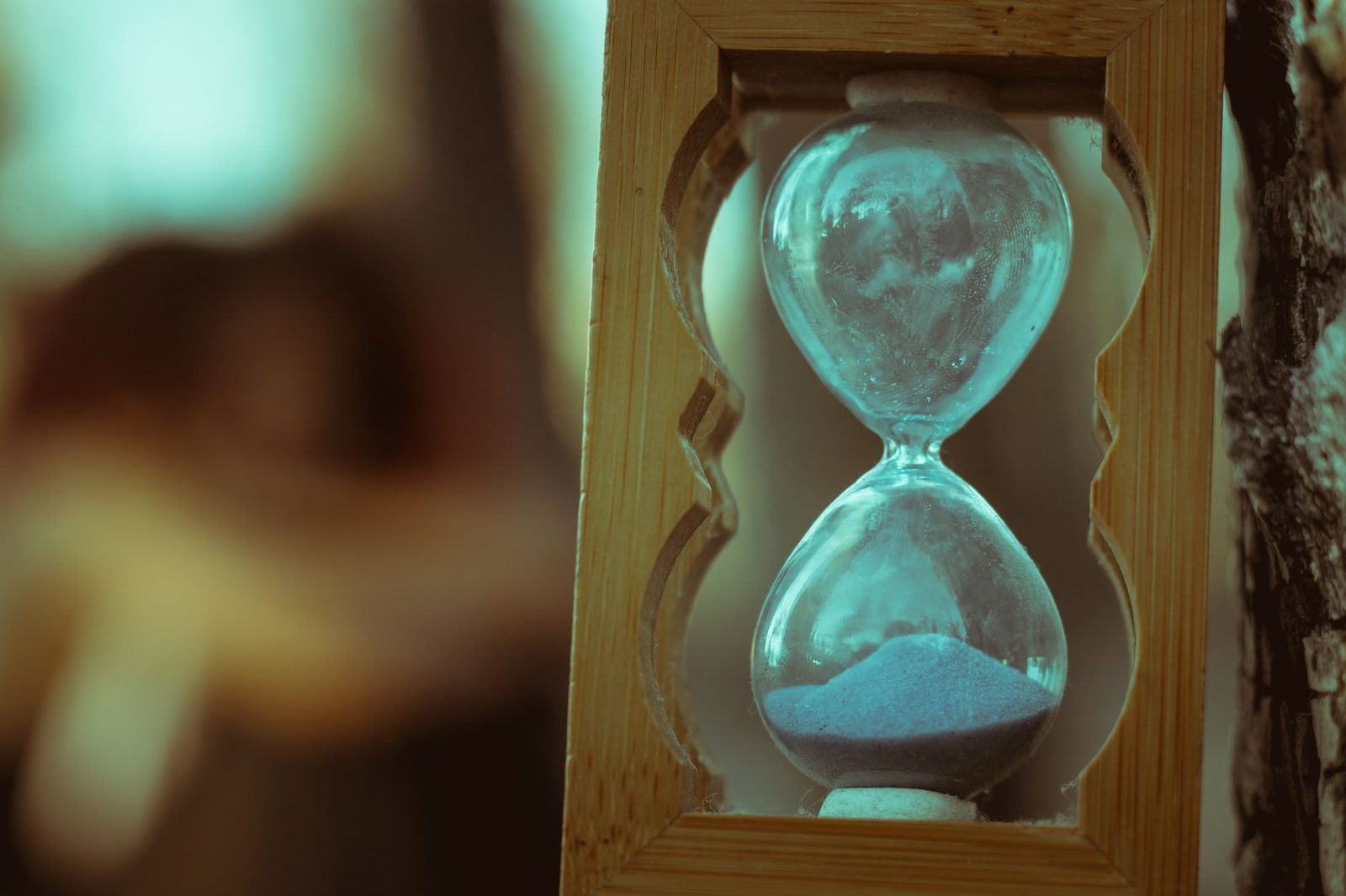 Reloj de arena de vidrio con arena en marco de madera sobre fondo natural.