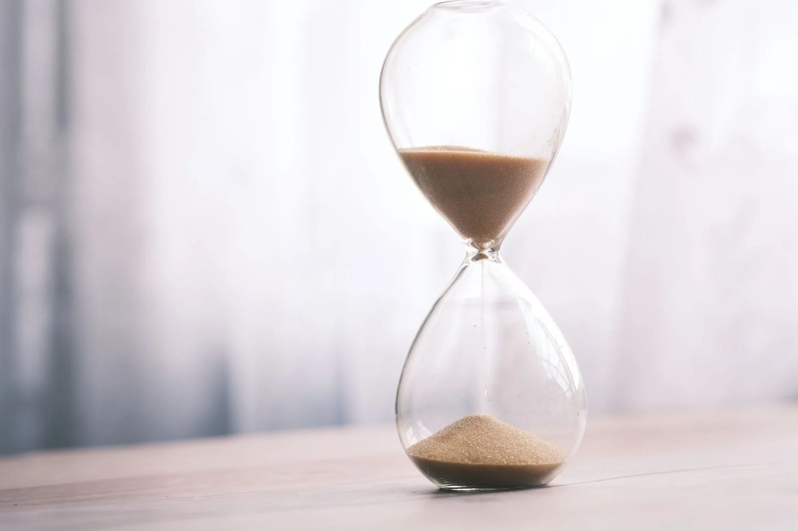 Reloj de arena minimalista con arena fina sobre un fondo suave y neutro, símbolo de tiempo y paciencia.