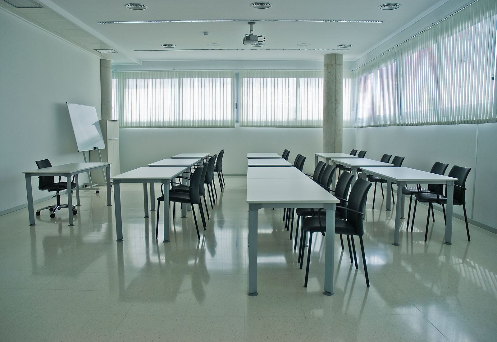 Sala de conferencias moderna con escritorios, sillas y pizarra blanca.