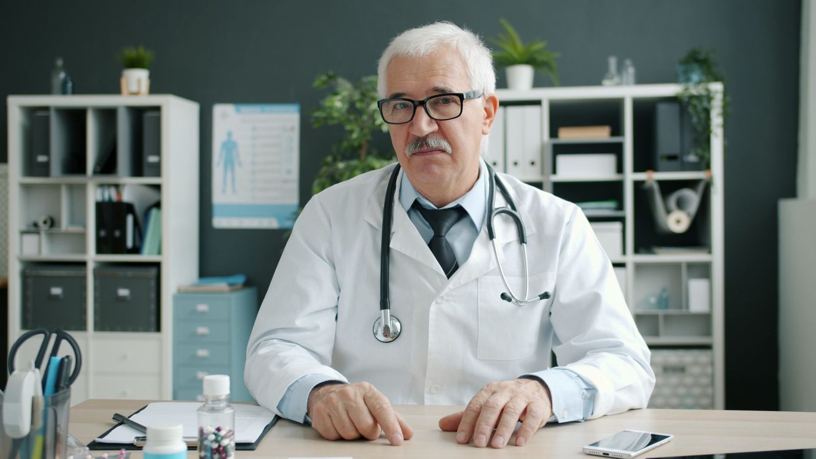 Senior doctor in office with medical equipment and patient files.