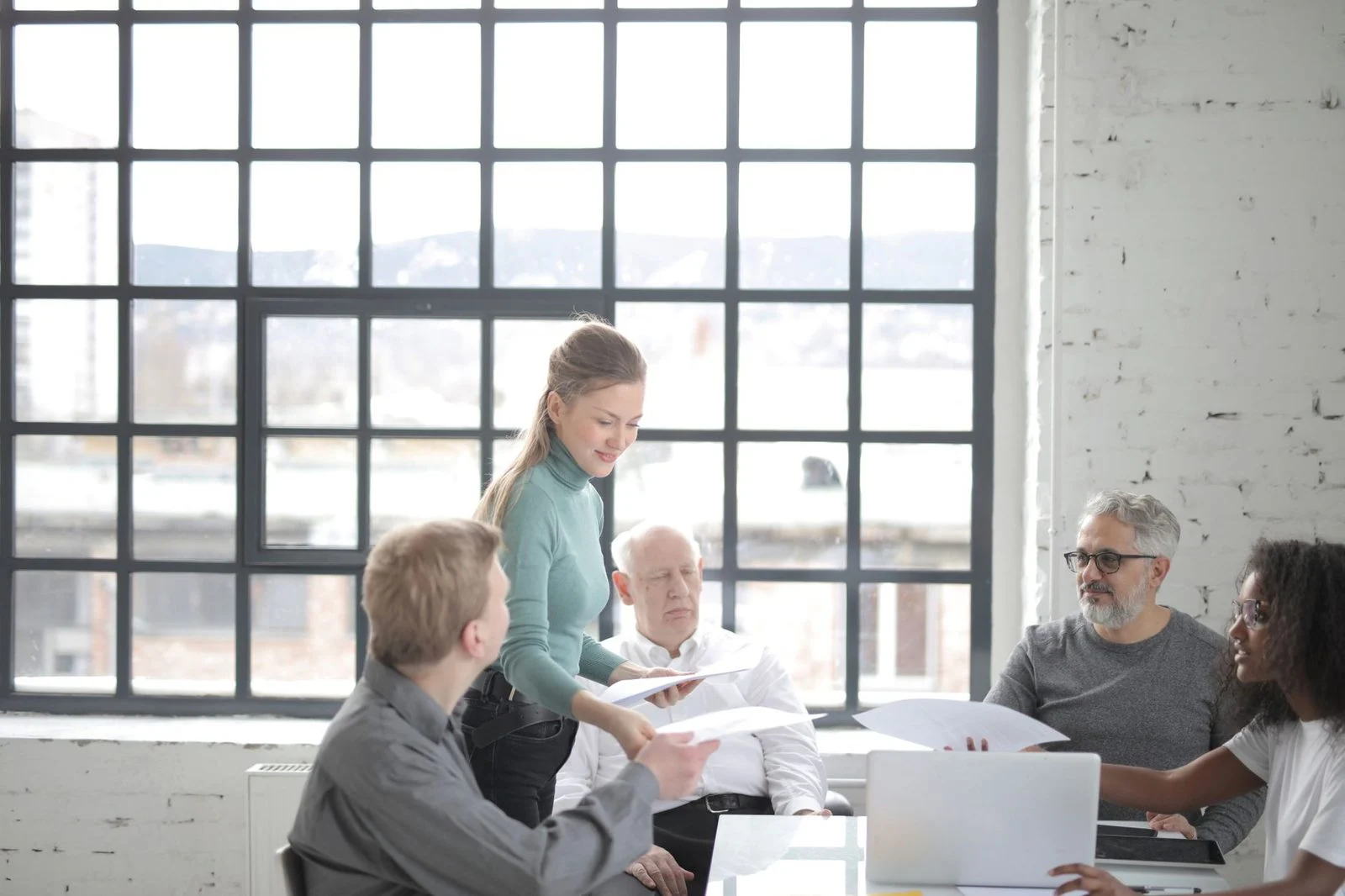 Several coworkers of different ages and backgrounds, in casual clothes, discuss a work plan around a table with a laptop.
