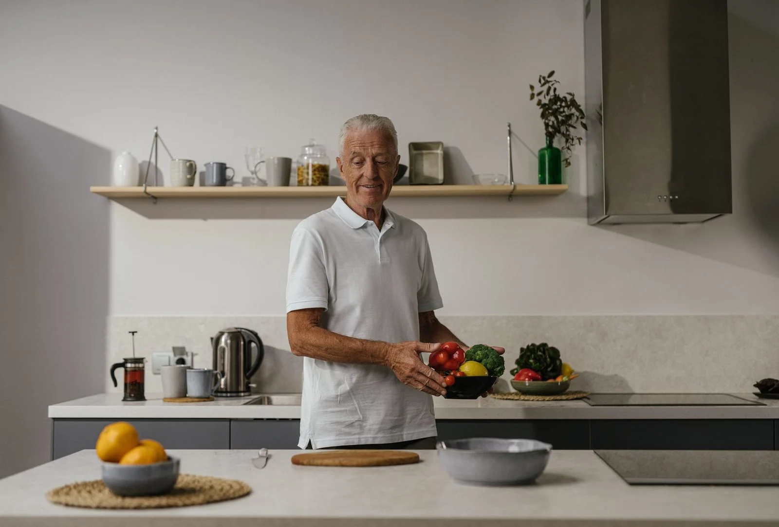 Smiling older man chopping vegetables at a bright, modern kitchen counter.