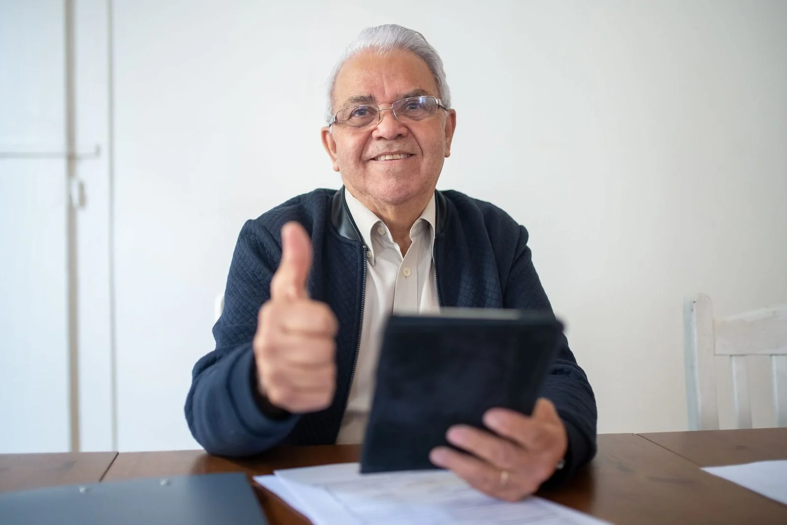 Smiling senior man sitting with a tablet and giving a thumbs up.