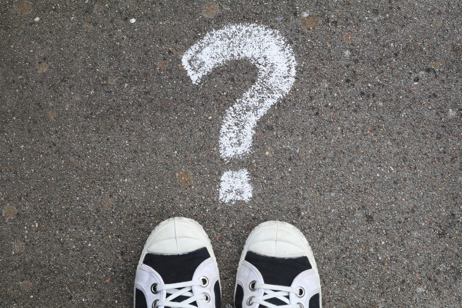 Sneakers on a pavement beside a chalk question mark.